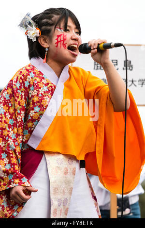 Close up de belle jeune femme japonaise annonceur, en yukata orange veste, parle dans le microphone à main au festival danse Yosakoi à Kumamoto. Banque D'Images