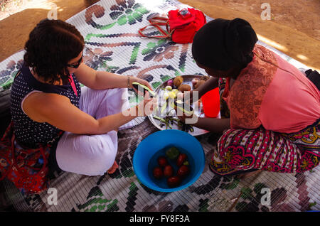 Deux femmes, l'une européenne et l'un d'Afrique, assis sur le sol, l'épluchage de légumes à Zanzibar, Tanzanie Banque D'Images