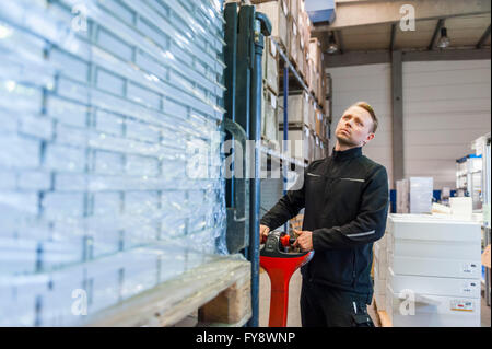 Travailleur dans le transport des marchandises sur les chariots d'entrepôt Banque D'Images