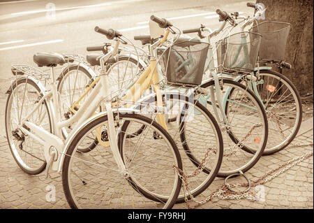 Quatre vélos garés sur le trottoir, enchaînés les uns aux autres. Effet vintage. Banque D'Images