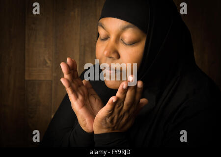 Femme musulmane africaine weiring un voile noir dans la prière Banque D'Images