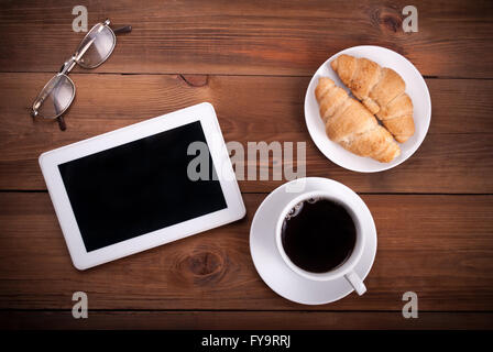 Ordinateur tablette croissants tasse de café verres sur un fond de bois. Vue d'en haut . Banque D'Images