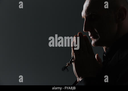 Silhouette of man holding rosary et priant sur fond noir Banque D'Images