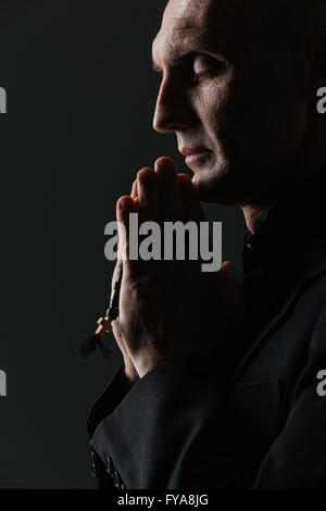 Man holding rosary et priant sur fond noir Banque D'Images