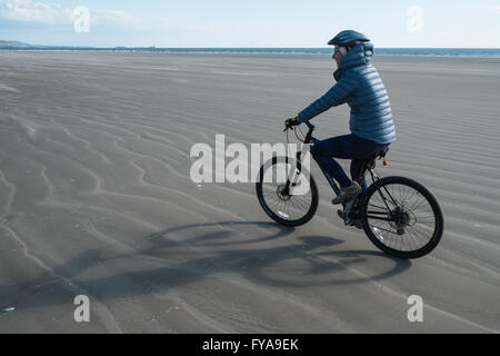 Femme,femme, vélo le long d'une partie de 8kms de long vide Pembrey Sands Beach sur une très venteux mais ensoleillé dimanche d'avril. Carmarthenshire, Pays de Galles, Royaume-Uni, Banque D'Images