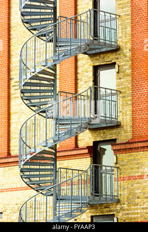 Escalier spirale allant d'un étage à l'extérieur d'un bâtiment en brique rouge et jaune. Portes en verre d'urgence menant à des mesures sont clos Banque D'Images