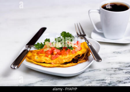 Close up d'omelette fraîchement préparé avec des tranches de tomate, oignon, persil, et de champignons dans le plat avec l'argenterie sur comptoir en marbre blanc Banque D'Images