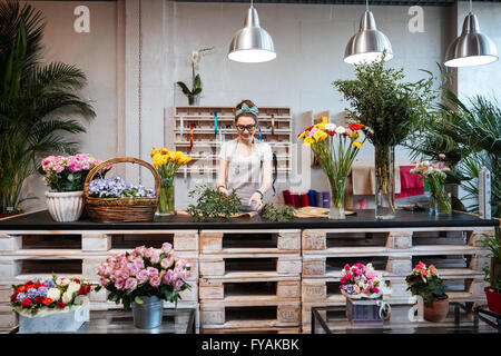 Smiling attractive young woman florist standing et travaillant dans le magasin de fleurs Banque D'Images