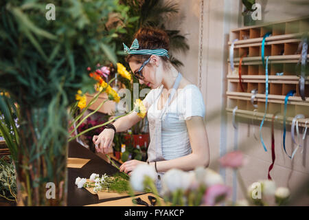 Jolie jeune femme grave et permanent fleuriste bouquet de fleurs blanches dans la boutique Banque D'Images