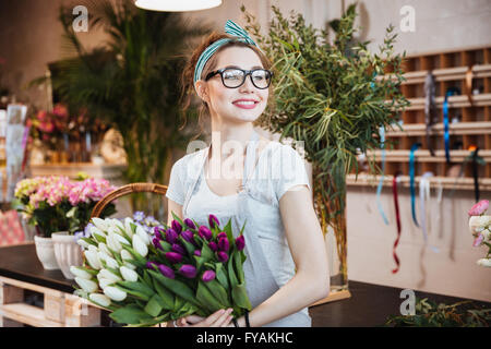 Cheerful attractive young woman florist holding white and purple tulips in flower shop Banque D'Images