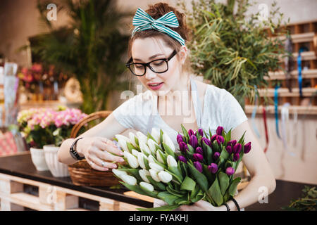 Cute belle jeune femme fleuriste à lunettes en prenant soin de tulipes dans le magasin de fleurs Banque D'Images