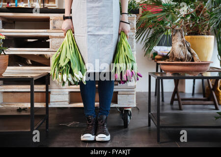 Gros plan du jeune femme fleuriste à sneakers debout et tenant deux bouquets de tulipes dans le magasin de fleurs Banque D'Images