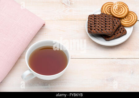 Tasse de thé et biscuits divers sur fond lumineux en bois Banque D'Images
