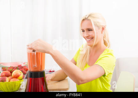 Une belle femme mature de préparer un smoothie ou un jus de fruits dans la cuisine. Banque D'Images