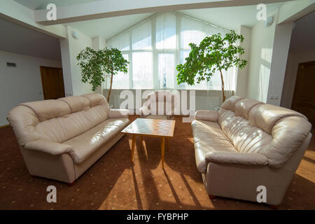 Hall de l'hôtel avec des arbres, des canapés en cuir, table basse Banque D'Images