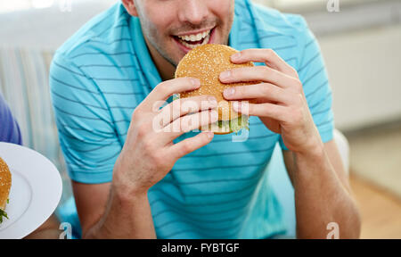 Close up of happy man eating hamburger à la maison Banque D'Images