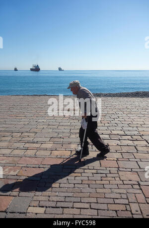 Vieil homme avec des béquilles marche sur front de mer. Espagne