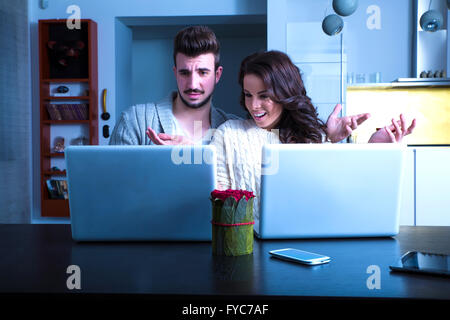 Un jeune couple en utilisant le soir leurs ordinateurs portables à la maison et la visite d'un site étrange. Banque D'Images