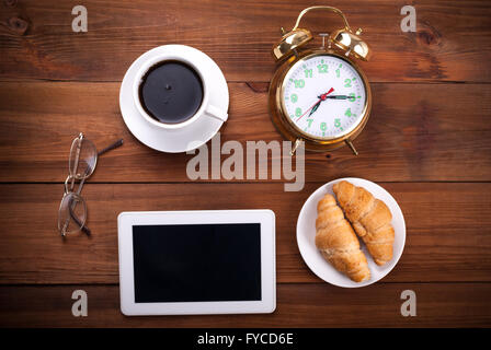 Bouilloire, réveil, verres, tablette numérique et les croissants sur la table en bois, vue du dessus. Banque D'Images