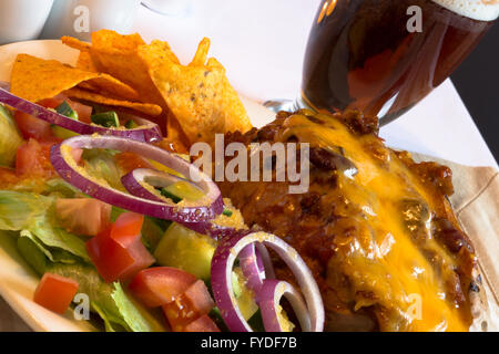 Anglais plat de pomme de terre au four avec du Chili de remplissage de boeuf garni de fromage râpé servi avec une salade et frites/chips Dorito Banque D'Images