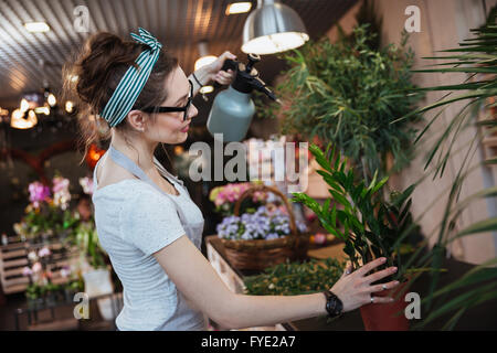 Smiling young woman florist standing et arrosage des plantes avec de l'eau pulvérisateur dans le magasin de fleurs Banque D'Images