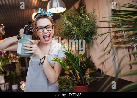 Jolie jeune femme drôle florist watering flowers et vers d'eau pulvérisateur sur vous Banque D'Images