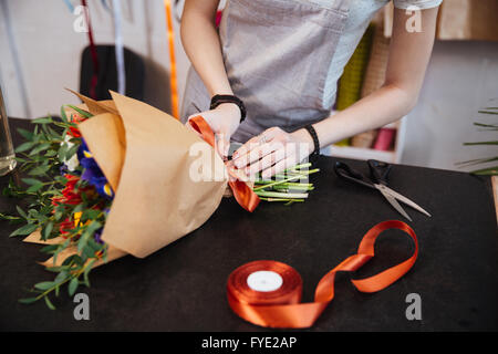 Jeune femme faisant fleuriste bouquet de fleurs à l'aide de ruban rouge sur tableau noir Banque D'Images