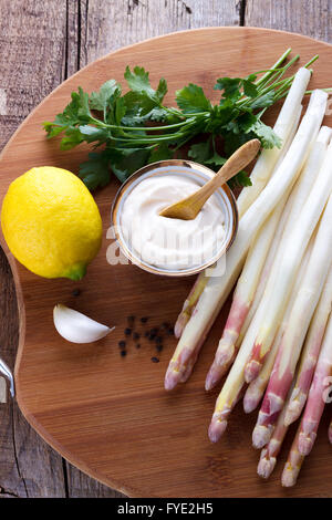 Asperges pelées et ingrédients pour une sauce sur planche de bois Banque D'Images