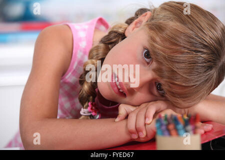 Petite fille aux craies resting head on desk Banque D'Images