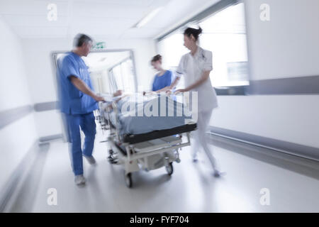 Une photographie d'un flou de mouvement senior female patient sur civière ou gurney poussés en pleine vitesse dans un couloir de l'hôpital Banque D'Images