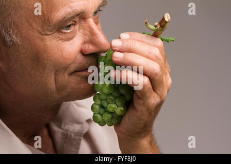 Portrait d'un agriculteur horizontale tenant un raisin vert fraîchement récolté dans sa main gauche et de le sentir Banque D'Images