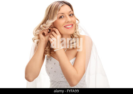 Jeune blonde bride mettre sur boucles d'oreilles et regardant la caméra isolé sur fond blanc Banque D'Images