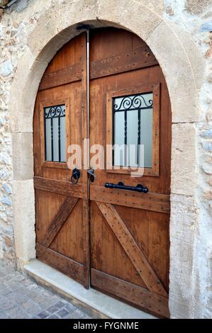 Une double porte en bois sombre sur un mur de pierre avec un arc, une fenêtre et des bars. Banque D'Images