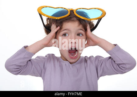 Petite fille hurlant avec d'énormes lunettes drôles sur la tête Banque D'Images