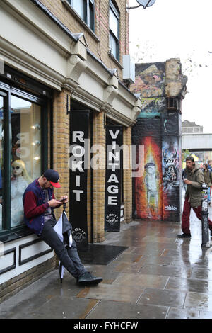 Un homme se penchant en dehors de la Rokit Vintage shop dans la région de la hanche de Shoreditch, London. Banque D'Images