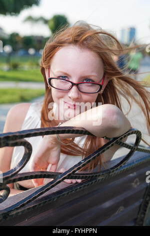 Belle jeune femme assise sur le banc de parc d'été Banque D'Images