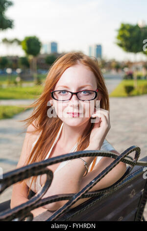 Belle jeune femme assise sur le banc de parc d'été Banque D'Images