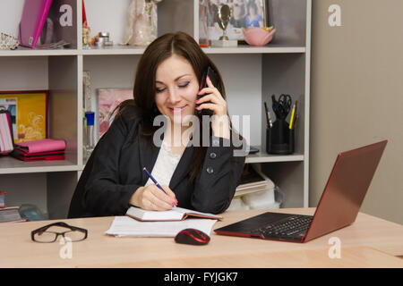 Femme d'affaires écrit dans un cahier et parlant au téléphone Banque D'Images