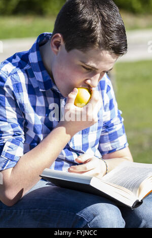 Été.le jeune homme de lire un livre dans l'air extérieur jaune avec Apple. Banque D'Images