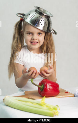 Girl playing cuire mettre une passoire sur la tête et tient en mains les oeufs Banque D'Images