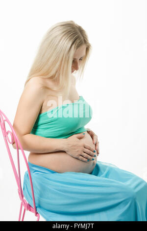 Jeune femme enceinte assise sur une chaise et à l'estomac à Banque D'Images