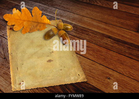 Old grunge papier avec l'automne les feuilles de chêne et de glands sur le fond en bois Banque D'Images