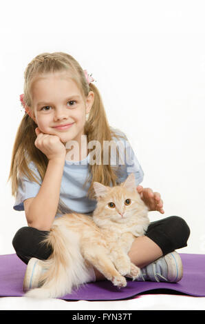 Fillette de six ans assis sur un tapis de l'athlète avec chat sur ses genoux Banque D'Images