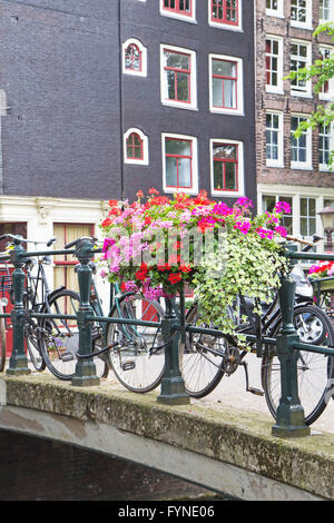 Pont sur canal à Amsterdam. Les bicyclettes sont standidg sur le pont. Le pont est décoré de fleurs. Banque D'Images