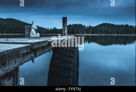 Fluffy toy bunny assis sur un quai. Rivage d'un lac de montagne Banque D'Images