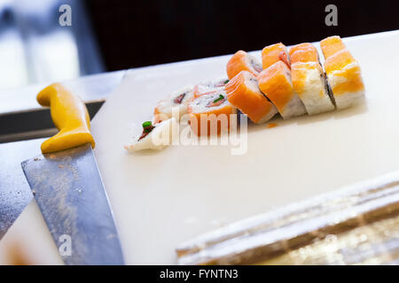 Rouleaux de sushi japonais traditionnel avec les saumons pondent sur blanc planche à découper, couteau chef. Selective focus Banque D'Images