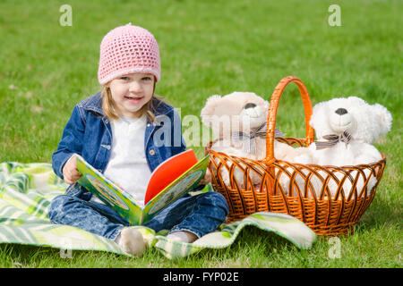 Happy little girl avec un livre sur un pique-nique Banque D'Images