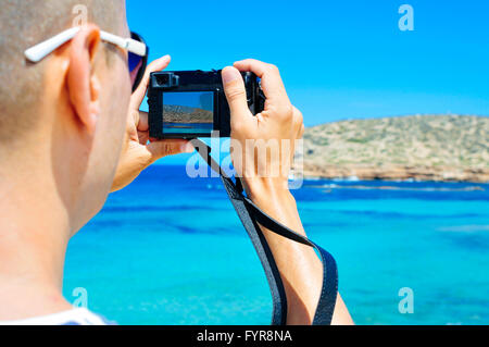 Libre d'un jeune homme de race blanche vue de derrière en prenant une photo de la mer Méditerranée et la côte de l'île d'Ibiza, Espagne Banque D'Images