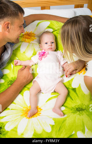 Maman et papa sont assis autour d'un bébé de deux mois qui est allongé sur le lit Banque D'Images