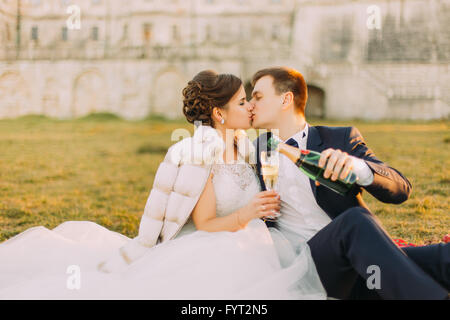 Les jeunes mariés assis sur le pique-nique, de boire des verres de champagne au mariage Banque D'Images